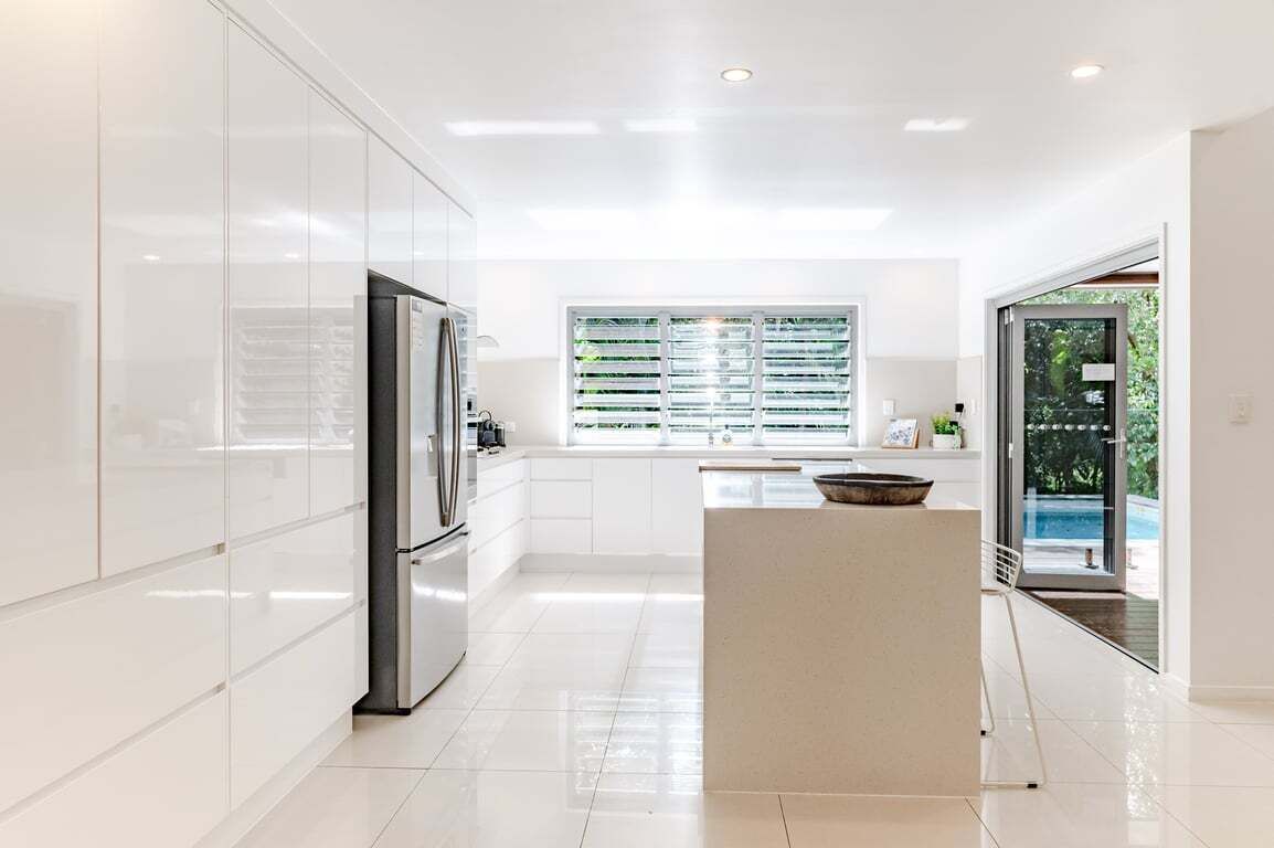 A modern kitchen with white cabinetry, a built-in oven, and a large window with blinds.