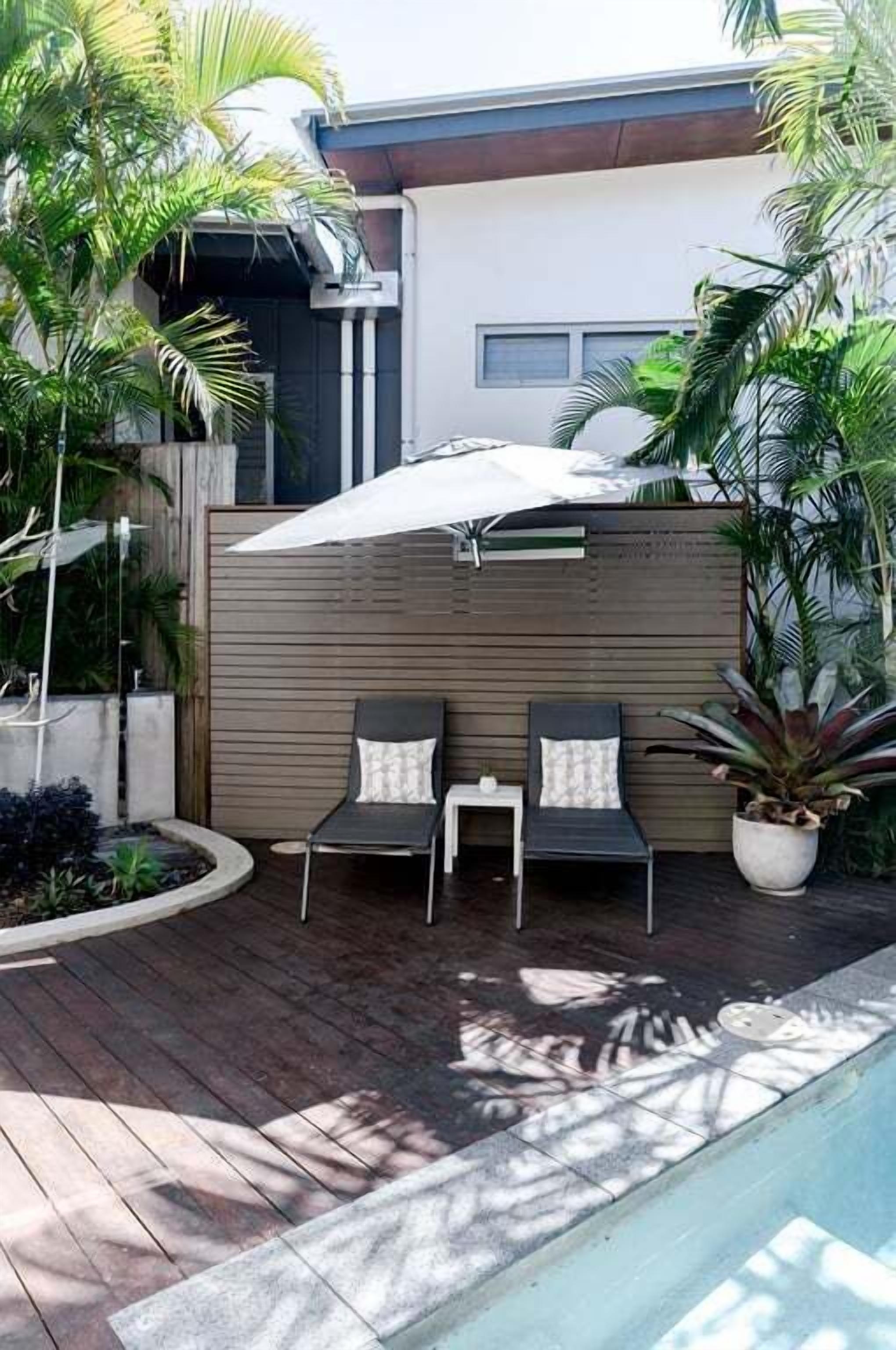 Une terrasse extérieure avec une piscine, deux chaises longues, une petite table et une plante en pot.