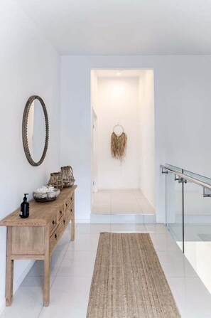 Ein modernes Interieur mit einem Holzkonsolentisch, einem gewebten Teppich, einem an der Wand befestigten Spiegel und einer Glastrennwand.