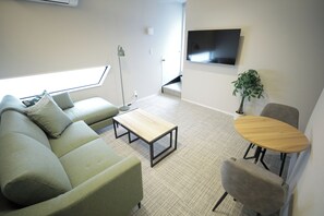 A modern living room with a sofa, a coffee table, a small table, a TV, and a plant.