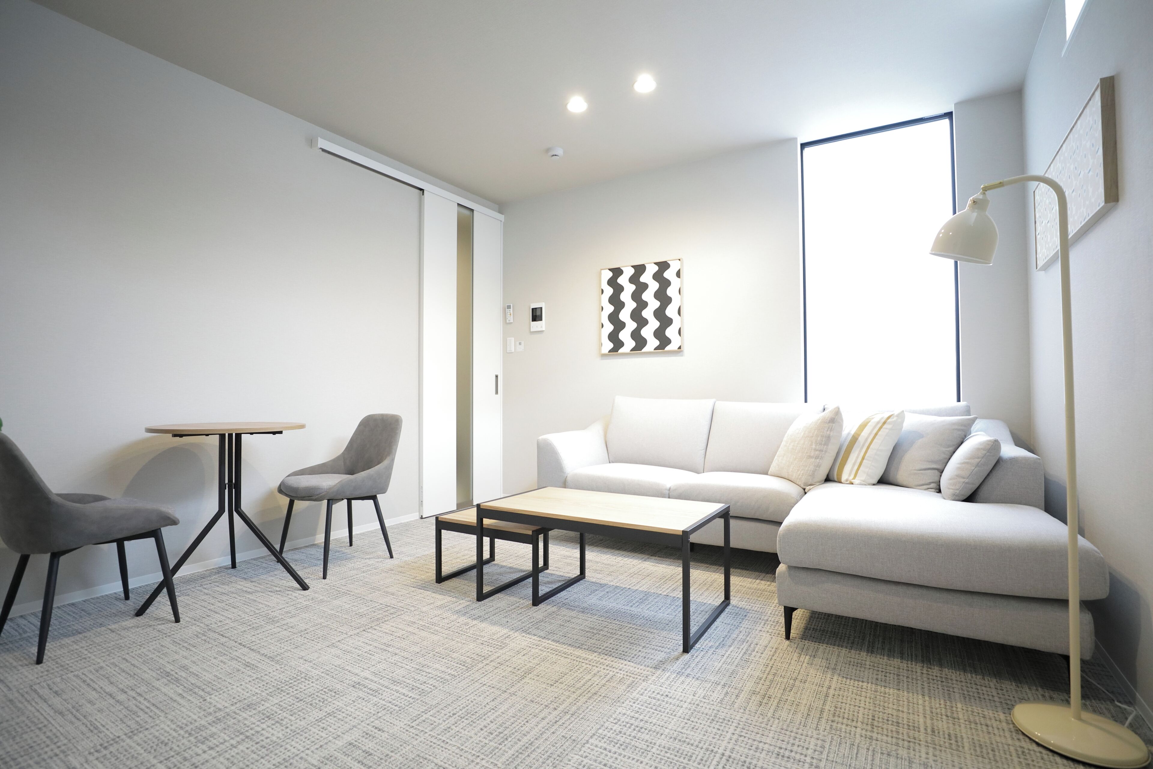 A modern living room with a sofa, two chairs, a coffee table, a floor lamp, and a wall-mounted artwork.