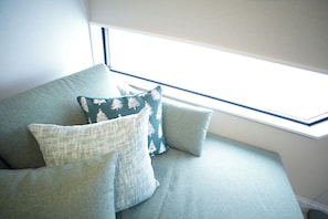 A corner of a room with a window, a sofa with cushions, and a wall.