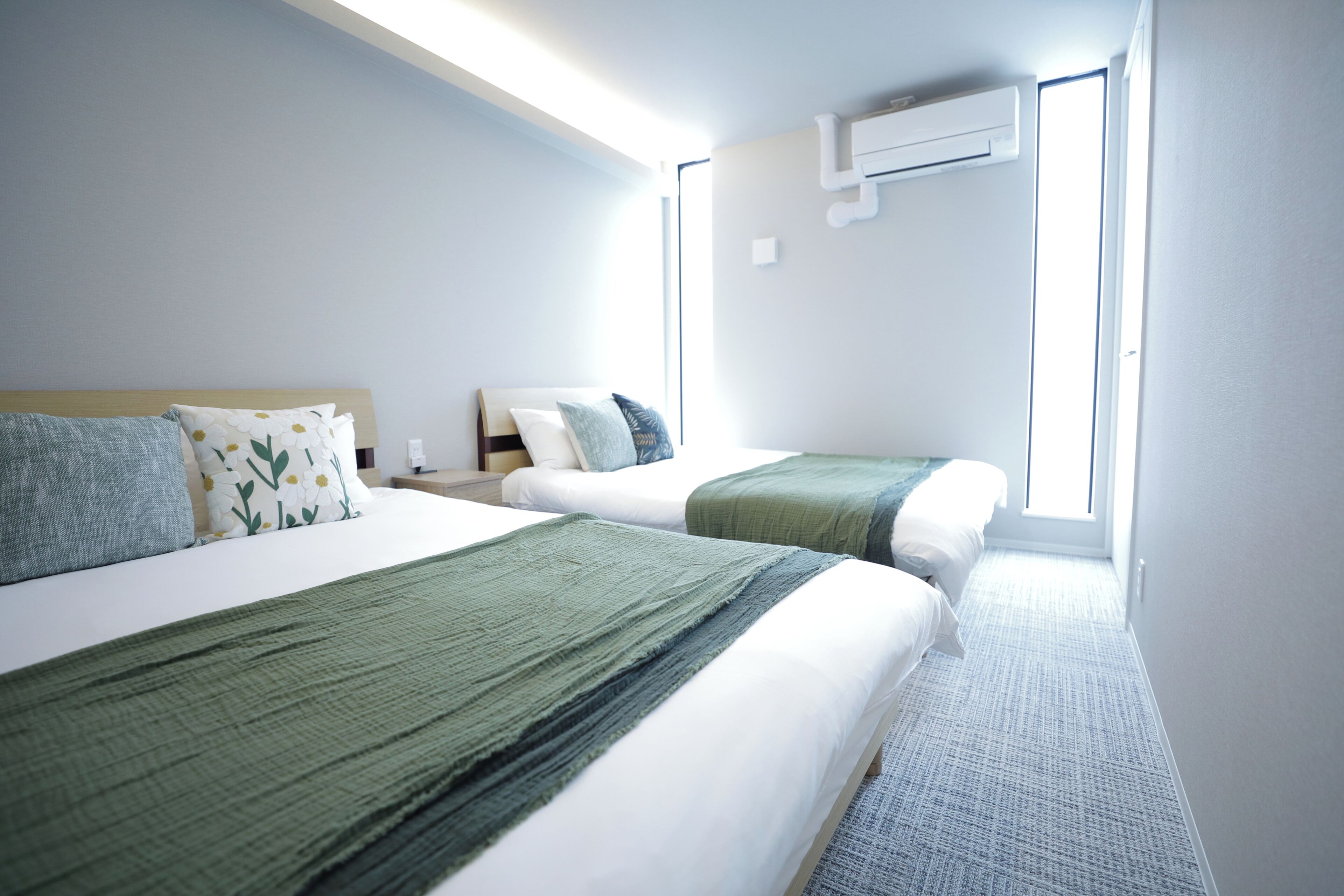 A hotel room with two beds, a window, and an air conditioning unit.