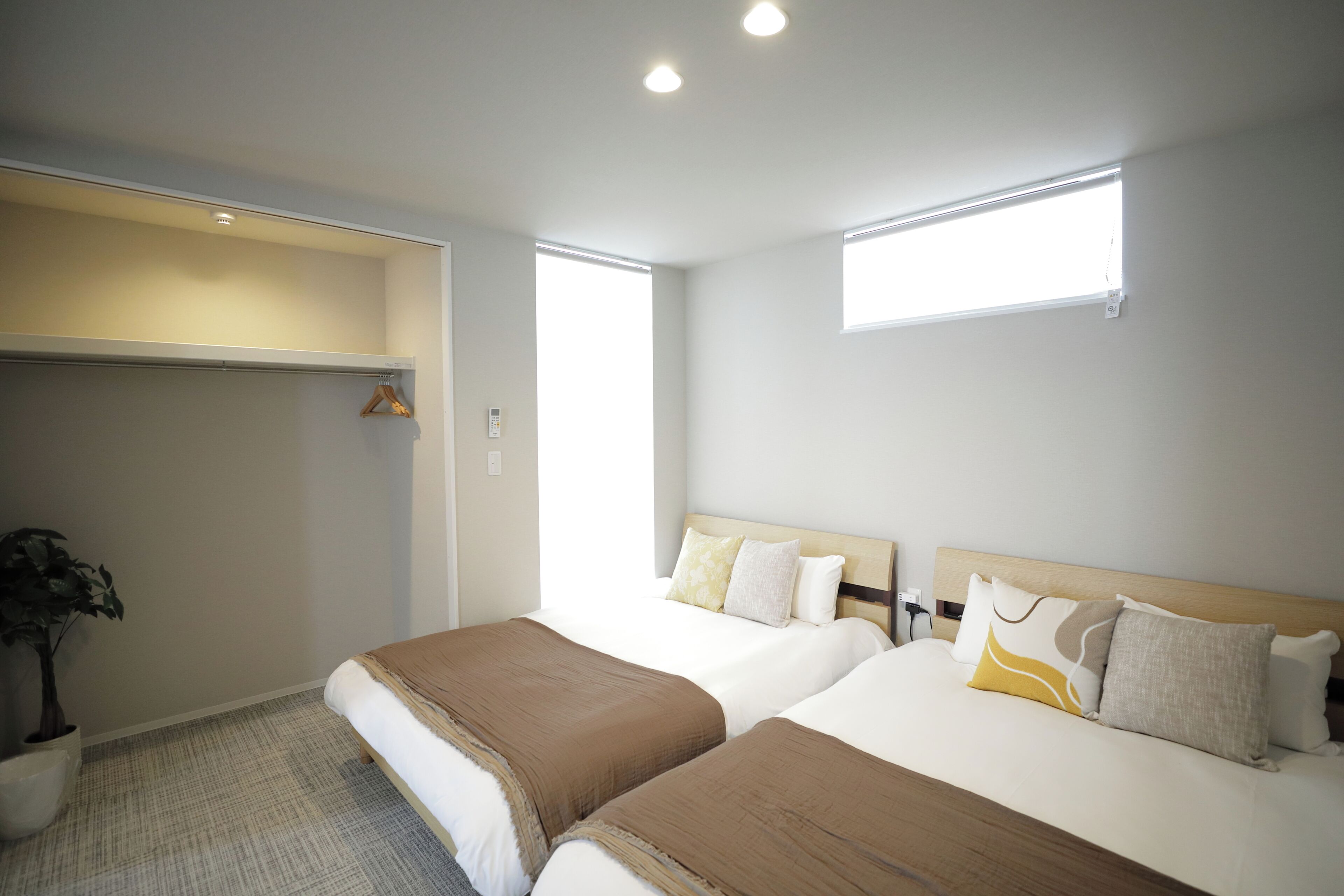 A hotel room with two beds, a closet, a potted plant, and a window.