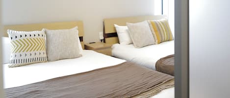 Una habitación de hotel con dos camas, una mesita de noche y una ventana.