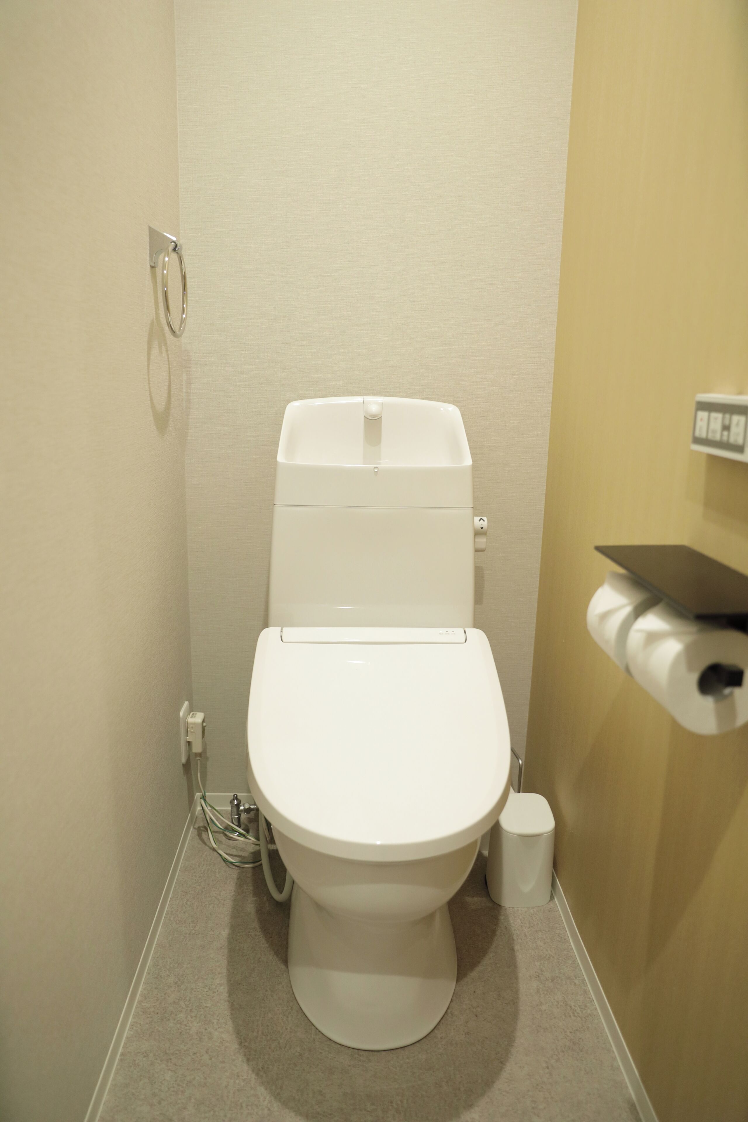 Des toilettes blanches classiques avec un réservoir, un porte-rouleau de papier toilette fixé au mur et une petite poubelle.