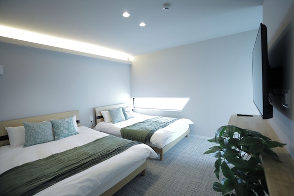 A modern hotel room with two beds, a large window, a flat-screen TV, and a potted plant.