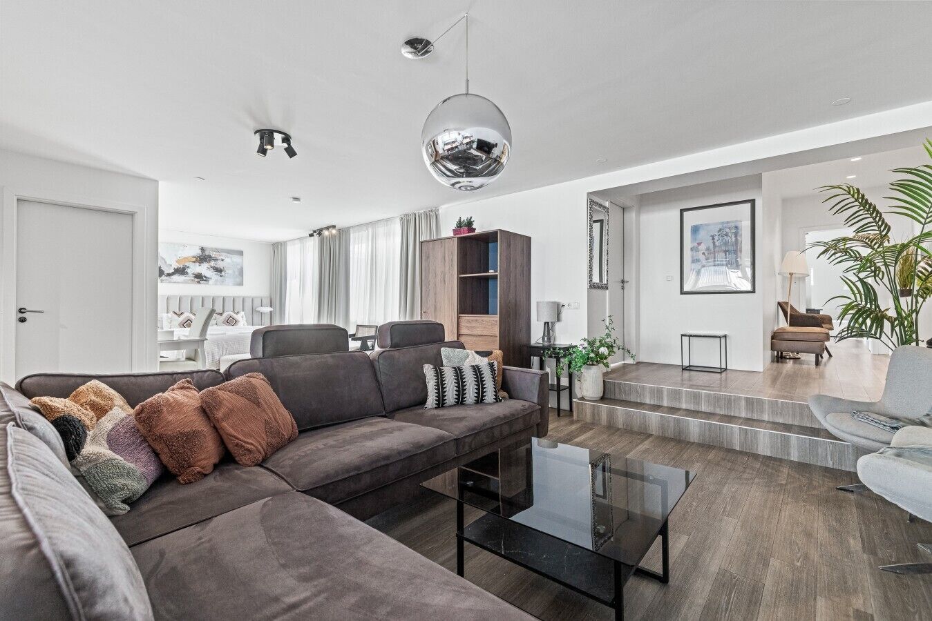 Una sala de estar moderna con un sofá modular, una mesa de centro de vidrio y una escalera que lleva a un nivel superior.