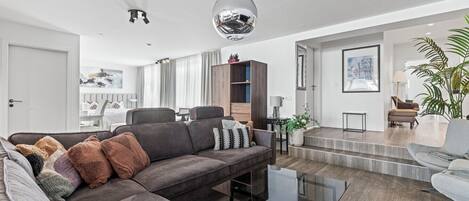 Una sala de estar moderna con un sofá modular, una mesa de centro de vidrio y una escalera que lleva a un nivel superior.