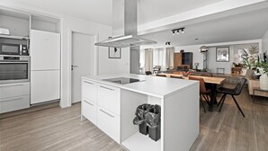 Et moderne køkken med en central ø, indbygget ovn og et rustfrit stål emfang.