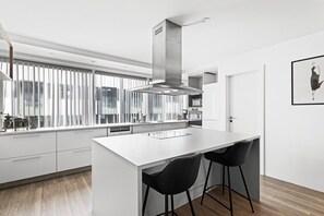 A modern kitchen with a large island, black bar stools, and a window with vertical blinds. - City-Center Gem with Prime Reykjavík Access (Reykjavík)