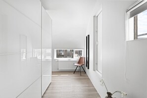 A narrow hallway with white walls, a radiator, a chair, and a window with a view of buildings. - City-Center Gem with Prime Reykjavík Access (Reykjavík)