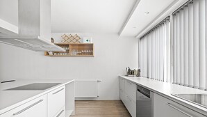 Et moderne køkken med hvide skabe, en indbygget ovn og et vindue med rullegardiner.