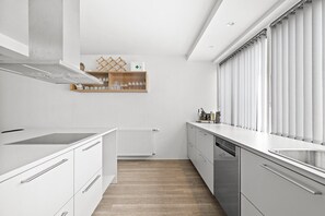 A modern kitchen with white cabinetry, a built-in oven, and a window with blinds. - City-Center Gem with Prime Reykjavík Access (Reykjavík)