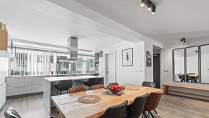 Et moderne køkken med en central ø, sorte stole og et træspisebord med en skål frugt.