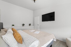 A modern bedroom with a bed, a television mounted on the wall, and a door leading to another room. - City-Center Gem with Prime Reykjavík Access (Reykjavík)