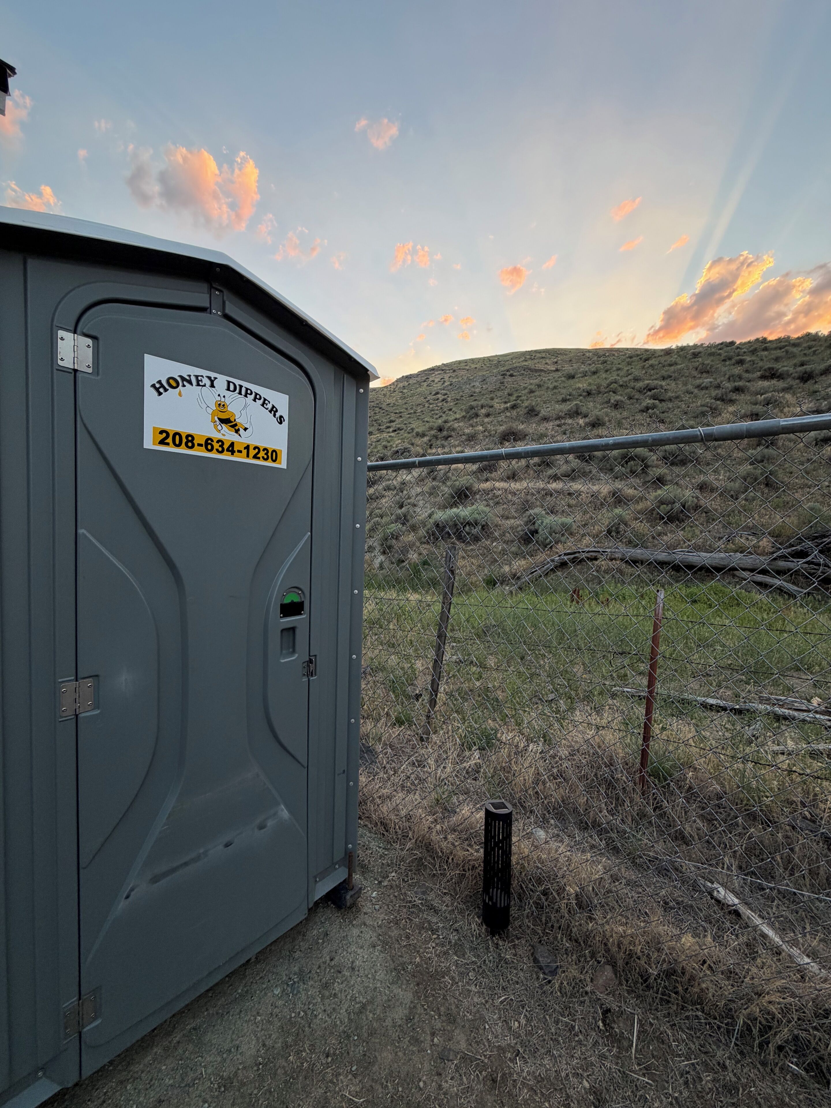A gray portable structure with a sign reading 'Honey Dippers' and a phone number.