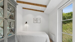 Een slaapkamer met een bed, een kledingkast, een radiator en een raam met uitzicht op groen.