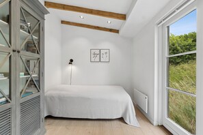 Ein Schlafzimmer mit Bett, Kleiderschrank, Heizkörper und einem Fenster mit Blick auf Grünflächen.
