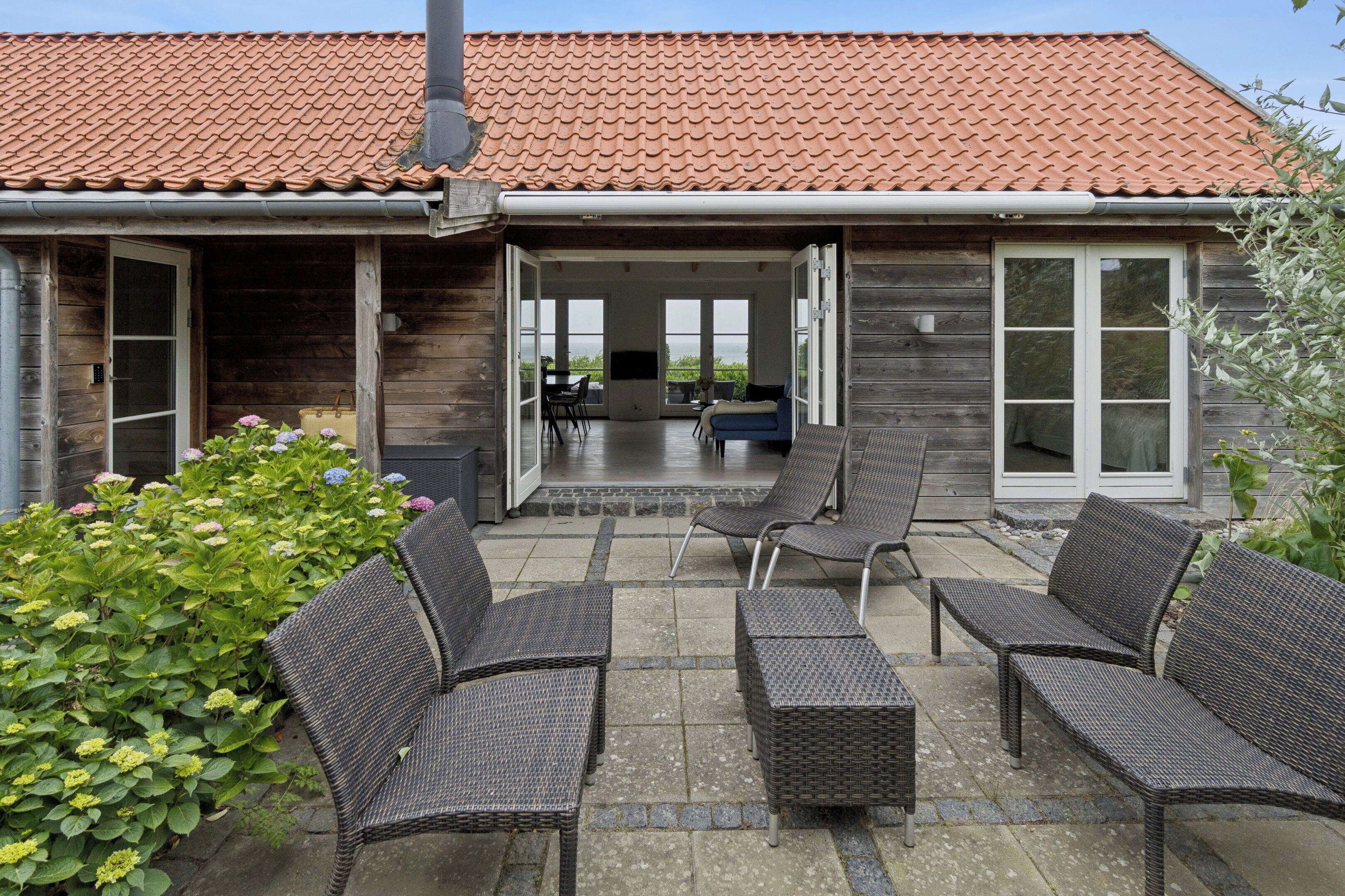 Een houten huis met een pannendak, een patio met rieten meubilair en uitzicht op zee.