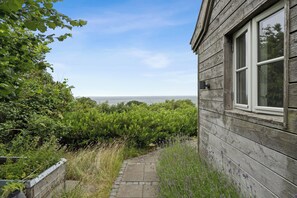 Un bâtiment en bois avec une fenêtre, un chemin de pierre et une végétation luxuriante.