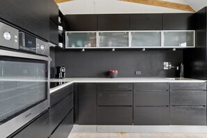 Une cuisine moderne avec des meubles de couleur sombre, une hotte de cuisinière en acier inoxydable et un four à micro-ondes encastré.
