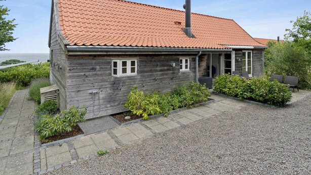 Een houten huis met pannendak, schoorsteen en een grindpad.