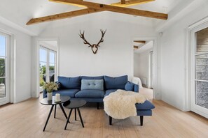A modern living room with a blue sofa, a round coffee table, and a mounted deer head on the wall. - Modern holiday home with sea view and terrace (Svaneke)