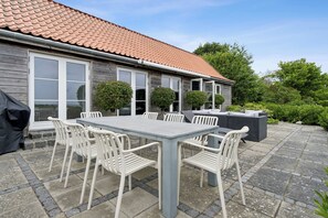 Une terrasse avec une table et des chaises, un barbecue et une maison avec un toit en tuiles et des fenêtres.