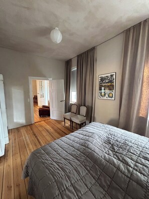 Une chambre à coucher avec un lit, une chaise, une porte donnant sur une autre pièce et un tableau accroché au mur.