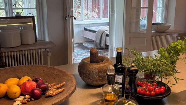 Una cocina con un tazón de madera lleno de frutas y verduras, un mortero de piedra y varias botellas.