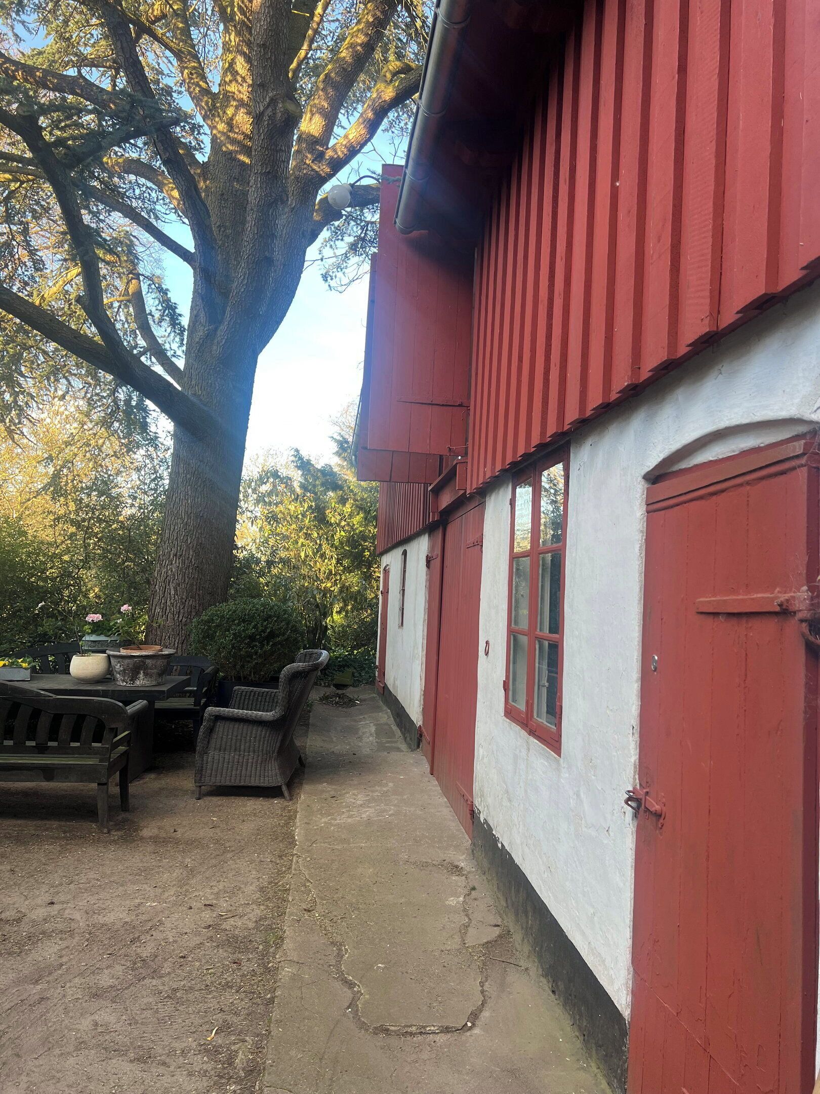 A rustic building with a red exterior, a large tree in front, and outdoor furniture.