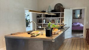 Cocina moderna con una isla central, piso de madera y vista a un dormitorio.