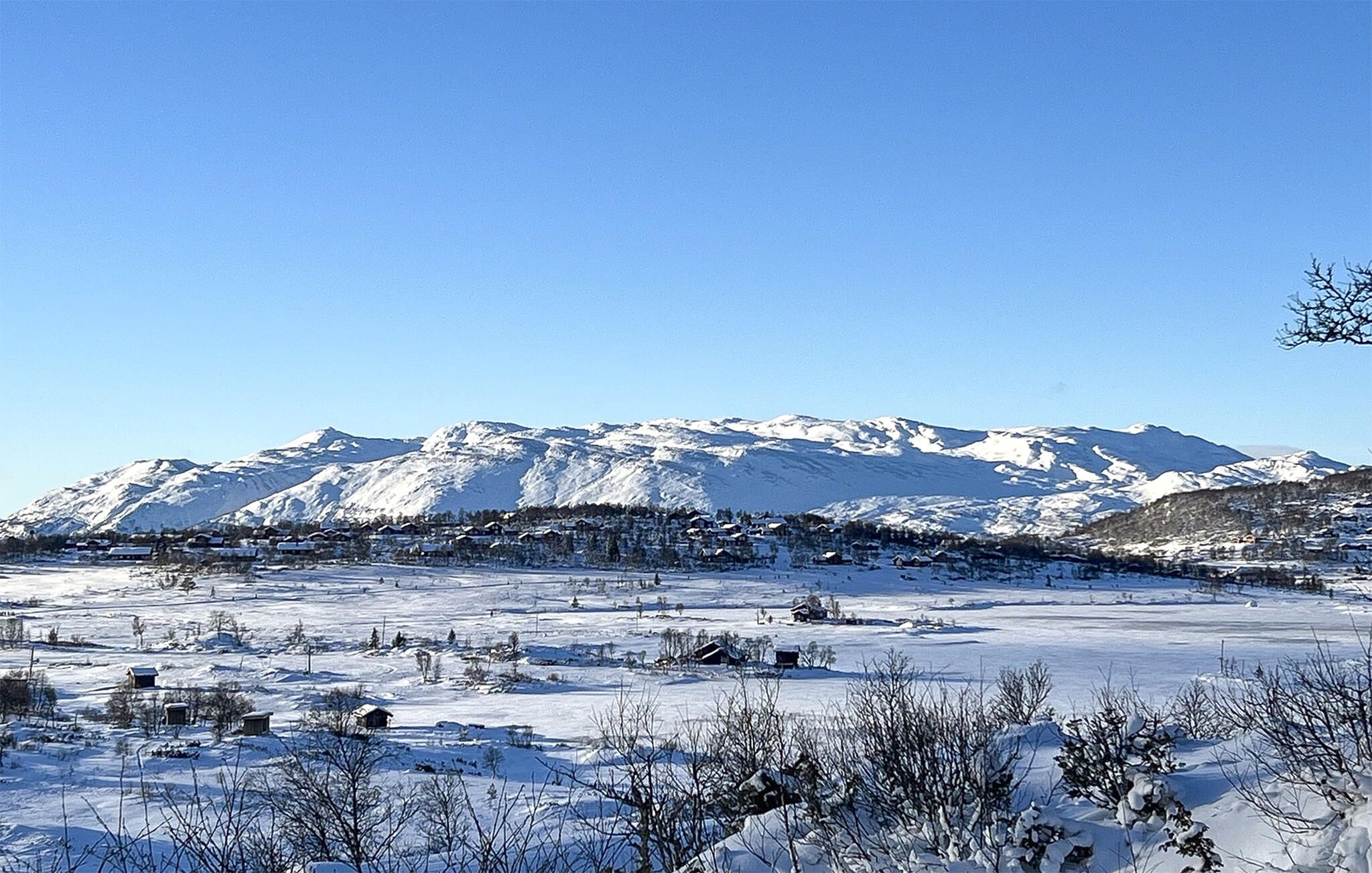 Ett snötäckt landskap med ett bergskedja i bakgrunden och några byggnader i förgrunden.