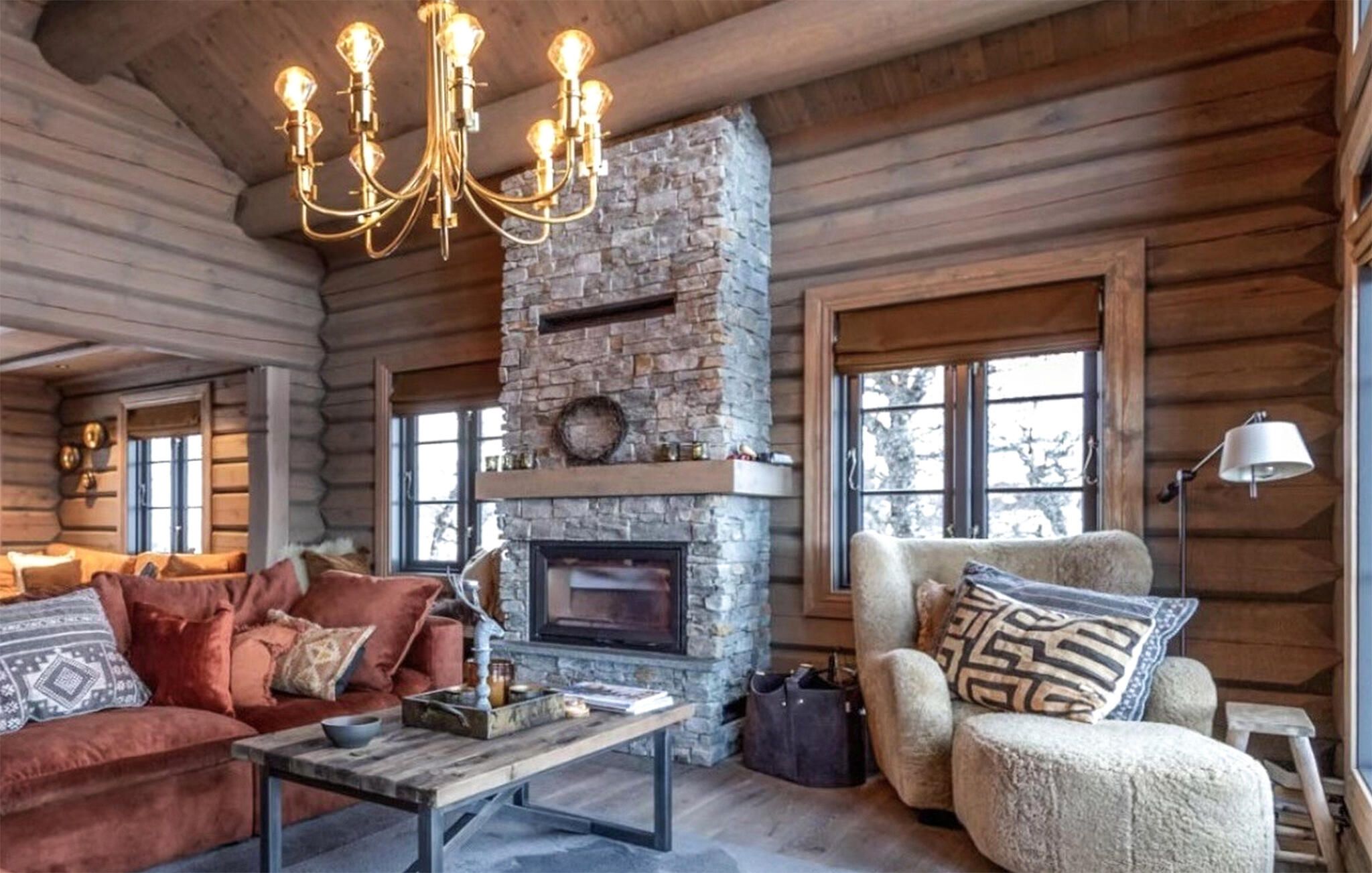 A log cabin interior with a stone fireplace, wooden walls, a chandelier, and a cozy seating area.
