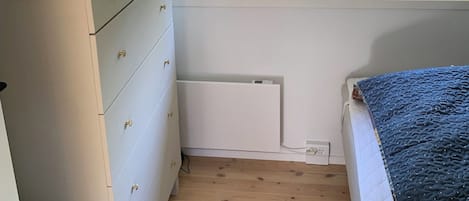 Un dormitorio con ventana, cómoda, radiador y cama.