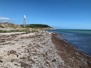 Una playa con costa rocosa, un muro de concreto y una colina con vegetación al fondo.