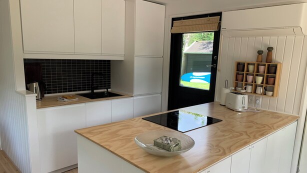 Een moderne keuken met witte kastjes, een zwart betegelde spatwand, een houten aanrecht, een ingebouwde kookplaat en een raam met uitzicht op een huis.