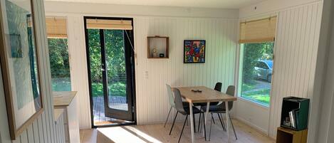 A room with a wooden floor, a dining table with chairs, a sofa, a bookshelf, and a door leading outside.