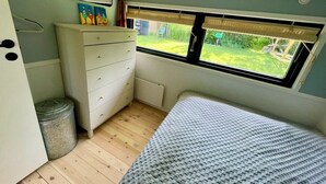 Een slaapkamer met een bed, een dressoir, een spiegel, een raam en een radiator.