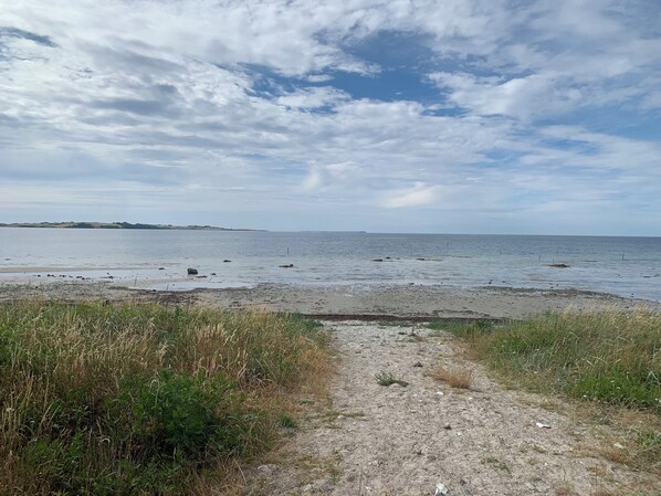 A coastal path leading to a beach with a clear sky and distant land.