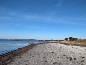 Una playa con cielo despejado, agua tranquila y colinas a lo lejos.