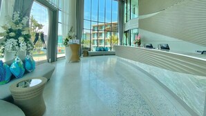 A modern hotel lobby with large windows, a curved ceiling, and a seating area with a sofa and a wicker chair.