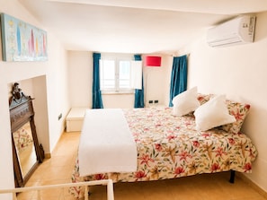 A bedroom with a bed, a window with curtains, a wall-mounted air conditioner, and a painting on the wall. - Casa Arcobaleno a Rio Marina (Rio Marina)