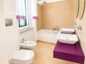 A bathroom with a bathtub, two sinks, a toilet, and a window with curtains. - Casa Arcobaleno a Rio Marina (Rio Marina)