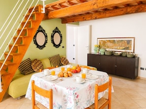 A dining area with a table set for breakfast, a staircase, a sofa, and a cabinet with kitchenware. - Casa Arcobaleno a Rio Marina (Rio Marina)