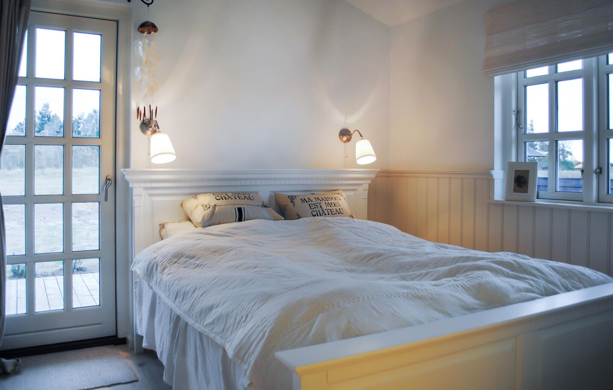Ein Schlafzimmer mit einem Bett, zwei Wandlampen, einer Tür mit Blick und einem Fenster.