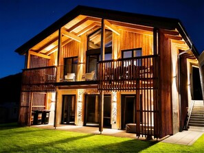 Ein zweigeschossiges Holzhaus mit einem Balkon, einem Steinkamin und einem gepflegten Rasen.
