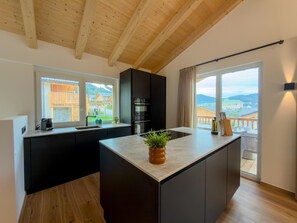 A modern kitchen with a central island, black cabinetry, and a view of a wooden deck through large windows. - Wonderful ski in-ski out chalet with Sauna (Sankt Lambrecht)