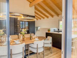 A modern dining area with a wooden table set for six, surrounded by chairs, and a kitchen visible in the background. - Wonderful ski in-ski out chalet with Sauna (Sankt Lambrecht)